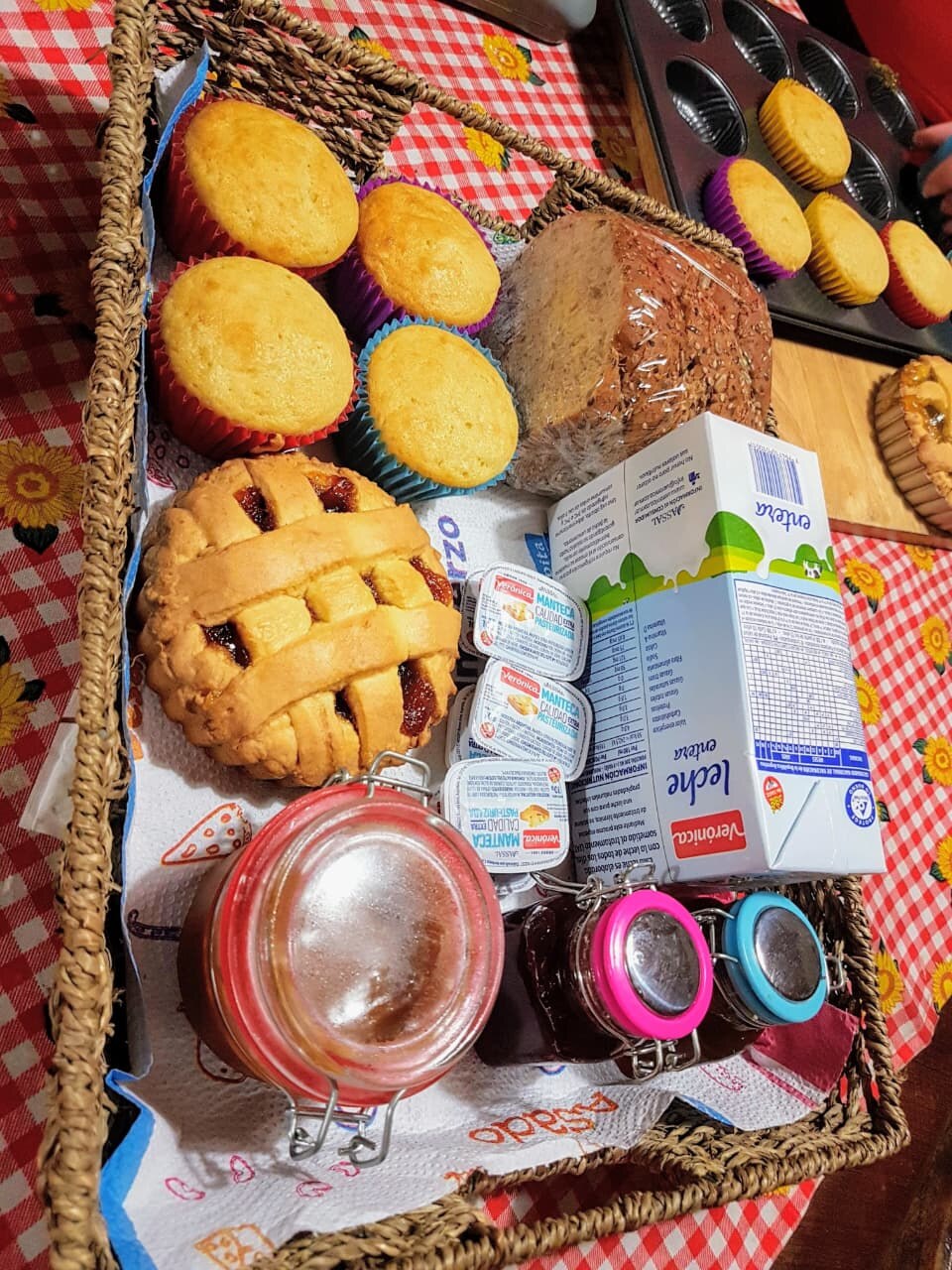 Canasta de desayuno con muffins, pastafrola, pan de semillas, leche, manteca y frascos de dulce