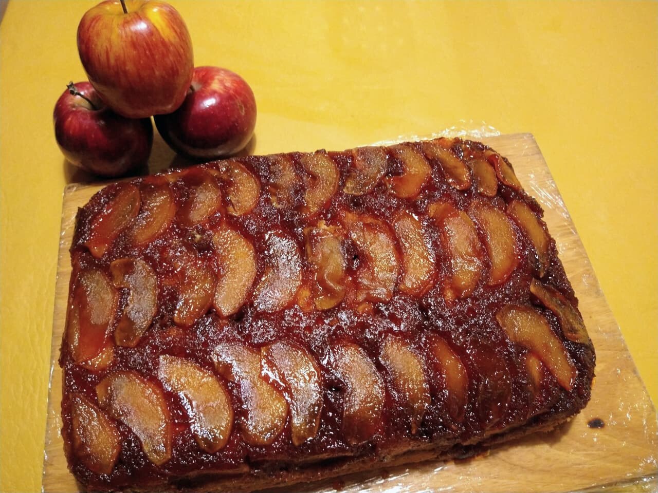 Torta de manzanas acaramelada sobre una tabla, con manzanas al costado